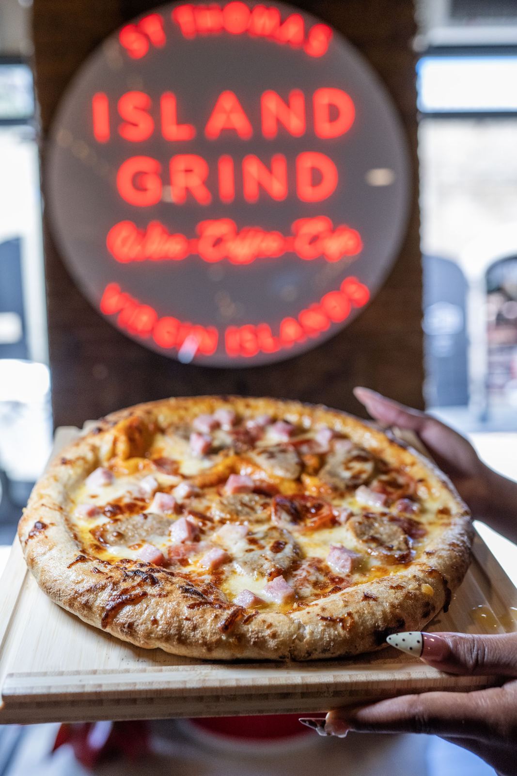 A whole pizza held up under the neon sign